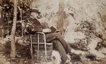 詹姆斯·朗兹在贝弗利农场，坐在户外的柳条椅上看书，狗在他脚边 照片graph